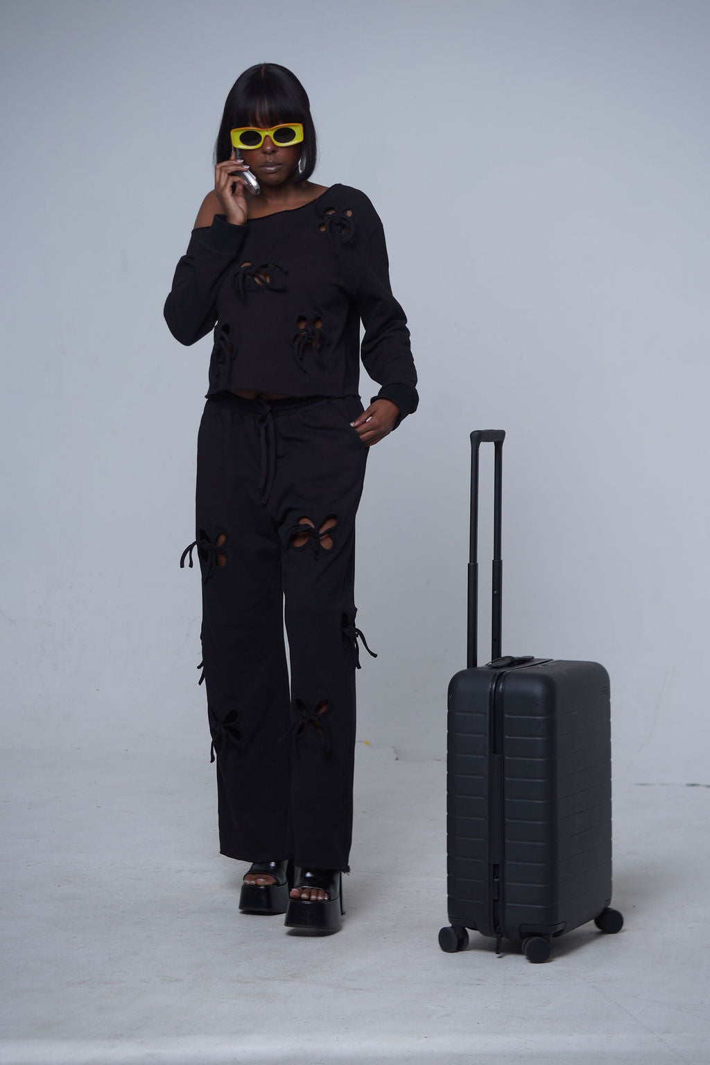 Dark Side Distressed Set in black — long sleeve distressed cutout sweatshirt with matching wide leg jogger pants, styled with platform sandals and yellow sunglasses,