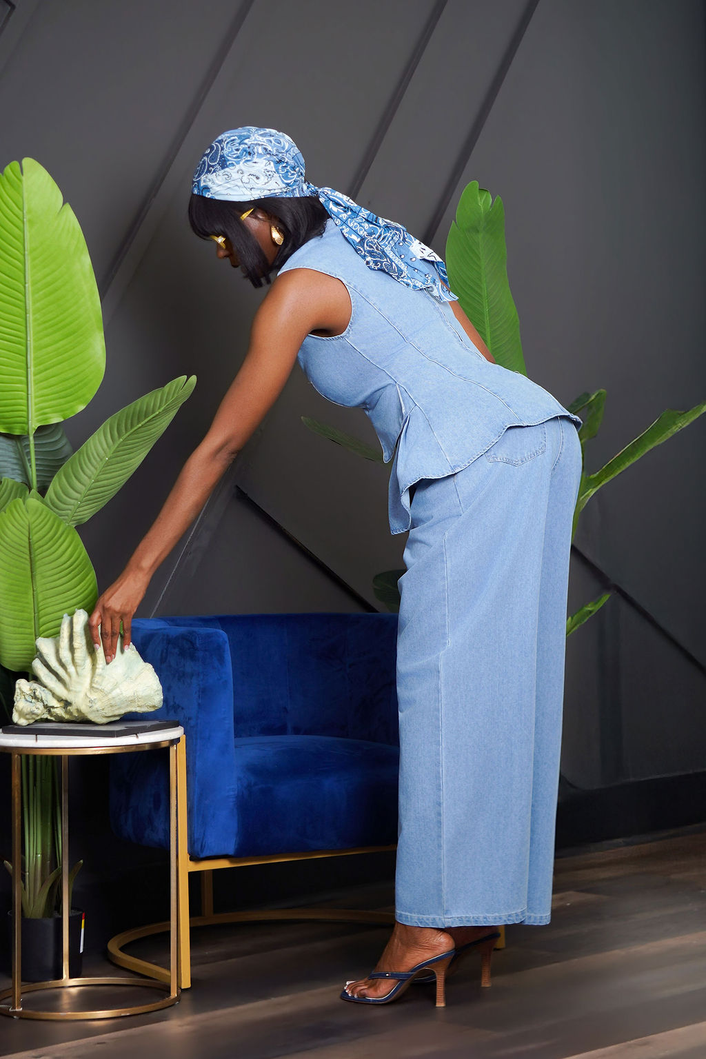 Indigo Peplum Pant Set in light wash denim — sleeveless structured peplum top with pleated ruffle hem, matching wide leg denim pants, styled with headscarf and yellow sunglasses