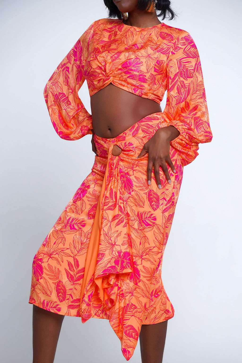 Island Twist Midi Set in orange and hot pink tropical leaf print — long sleeve twist knot crop top with balloon sleeves and matching wrap midi skirt with ring waist detail