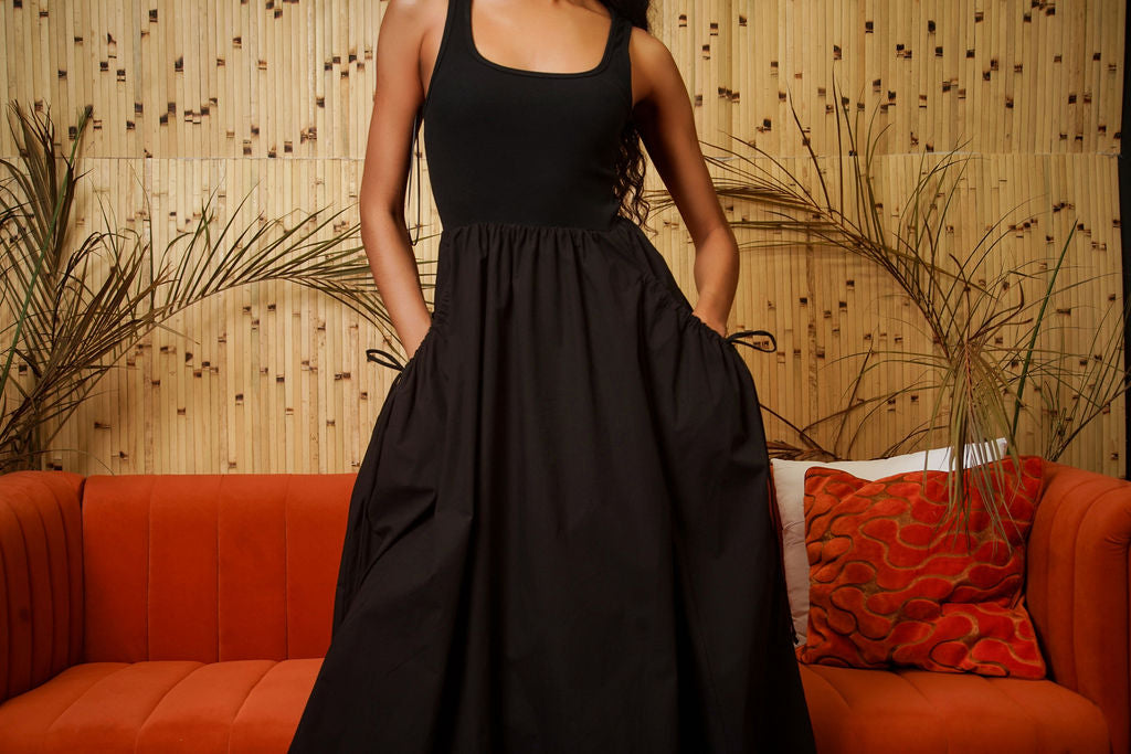 Model wearing Sun-Day black dress with pockets — square neckline, full skirt, styled with red cowboy boots, full length front view